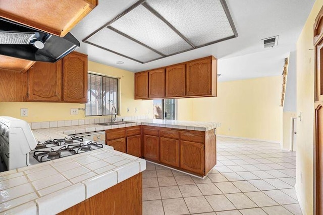 kitchen featuring tile countertops, visible vents, brown cabinetry, a sink, and a peninsula