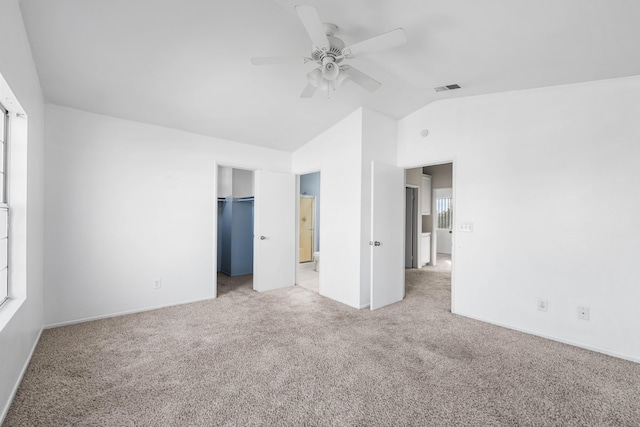 unfurnished bedroom with a walk in closet, lofted ceiling, light colored carpet, visible vents, and ceiling fan