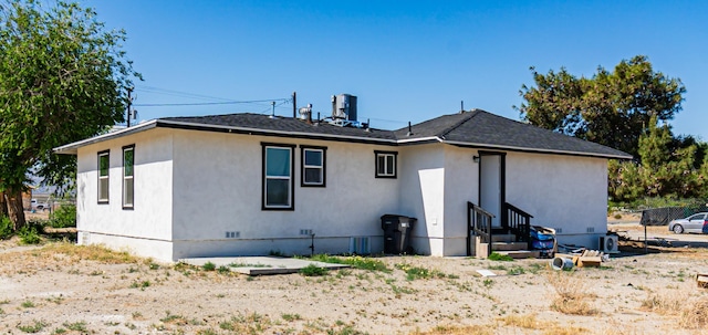rear view of house featuring entry steps, central air condition unit, and stucco siding
