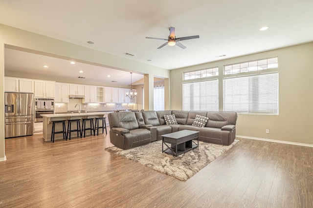 living room featuring ceiling fan with notable chandelier, visible vents, baseboards, and wood finished floors