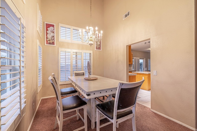 dining space with baseboards, visible vents, a high ceiling, light colored carpet, and a chandelier