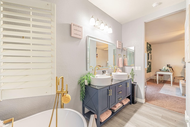 bathroom with a sink, a freestanding bath, wood finished floors, and double vanity