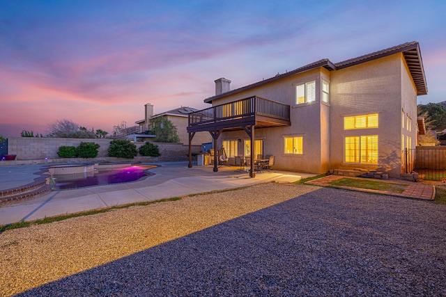 back of house at dusk with stucco siding, a patio, fence, a fenced in pool, and a balcony