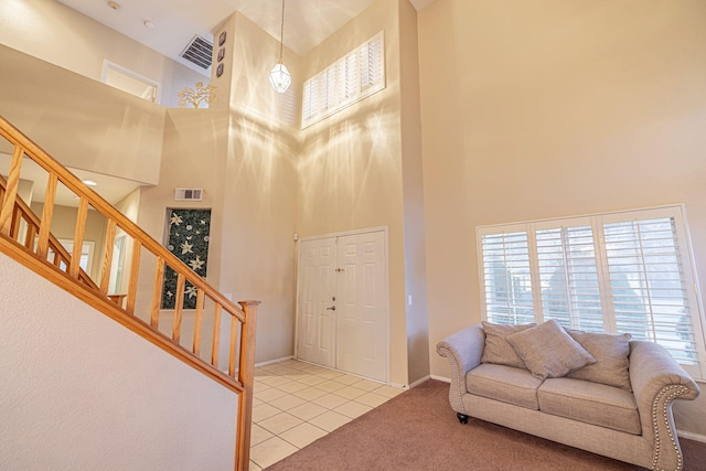 carpeted living room featuring stairs, a high ceiling, baseboards, and visible vents