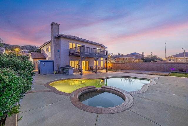 pool at dusk featuring fence, a pool with connected hot tub, and a patio area