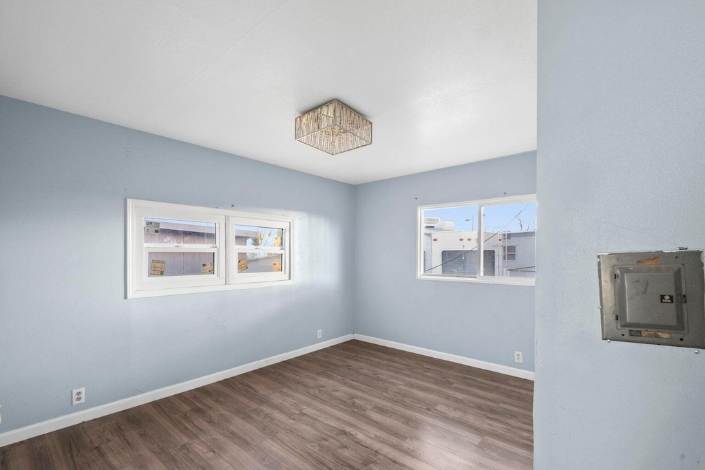 spare room featuring baseboards, wood finished floors, and electric panel