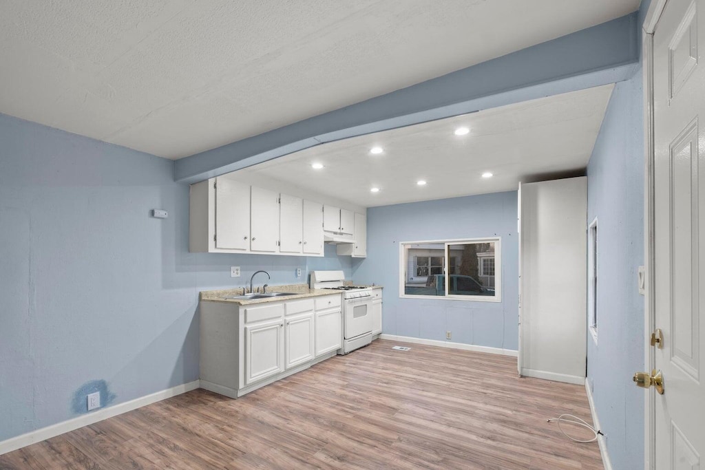 kitchen featuring baseboards, gas range gas stove, recessed lighting, and light wood-style flooring