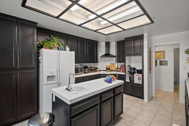 kitchen with sink, stainless steel appliances, wall chimney range hood, a kitchen island with sink, and light tile patterned flooring