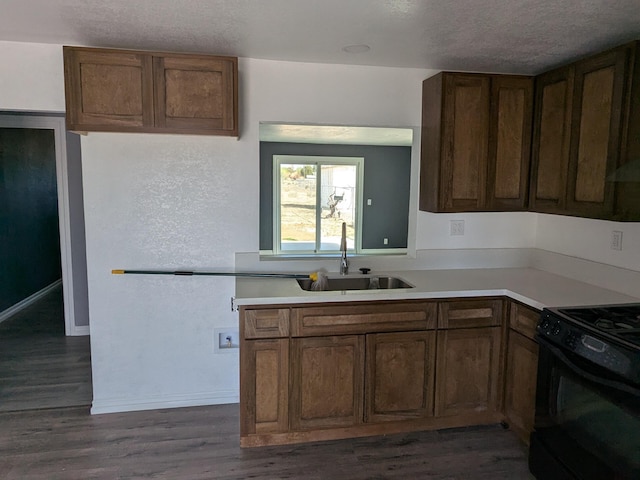 kitchen with black gas range oven, light countertops, a sink, and dark wood-style flooring