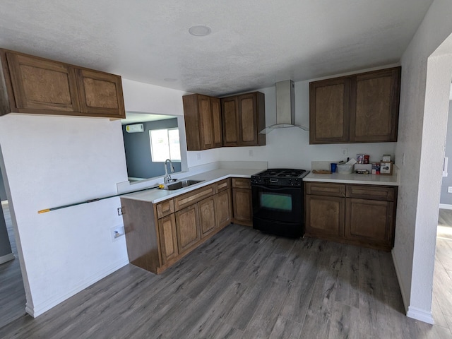 kitchen featuring light countertops, light wood-style flooring, a sink, wall chimney range hood, and black gas range