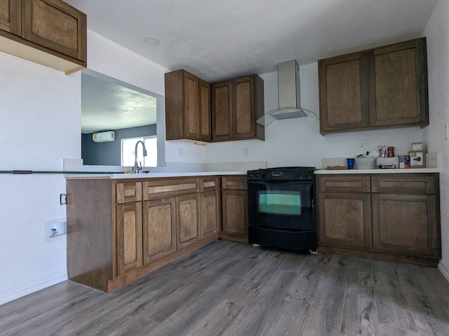 kitchen with light countertops, a sink, wood finished floors, wall chimney range hood, and black electric range