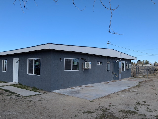 back of house featuring a wall mounted AC, stucco siding, and a patio