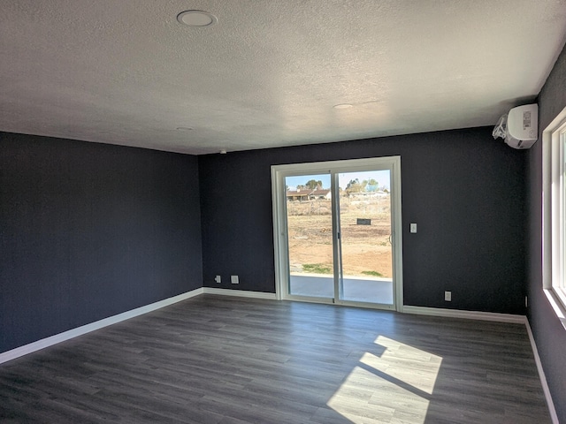 spare room featuring a wall unit AC, a textured ceiling, baseboards, and dark wood finished floors
