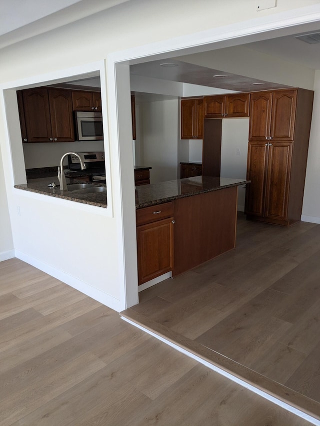 kitchen featuring visible vents, a peninsula, light wood finished floors, appliances with stainless steel finishes, and a sink
