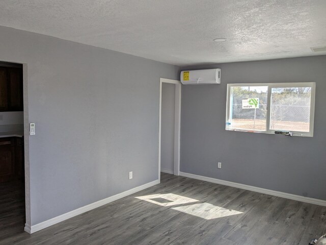 unfurnished room featuring a wall mounted AC, baseboards, a textured ceiling, visible vents, and wood finished floors