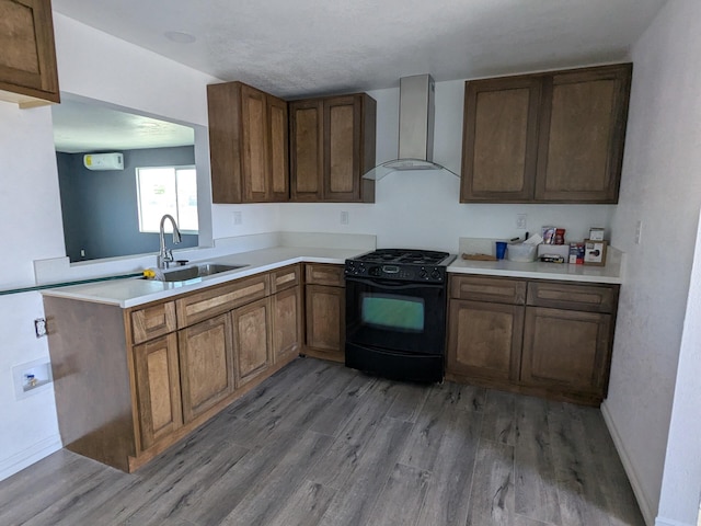 kitchen featuring light countertops, a sink, wall chimney exhaust hood, black gas range, and light wood-style floors
