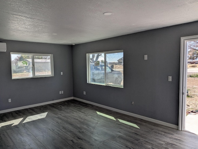 spare room featuring baseboards, a wall unit AC, dark wood-type flooring, and a textured ceiling