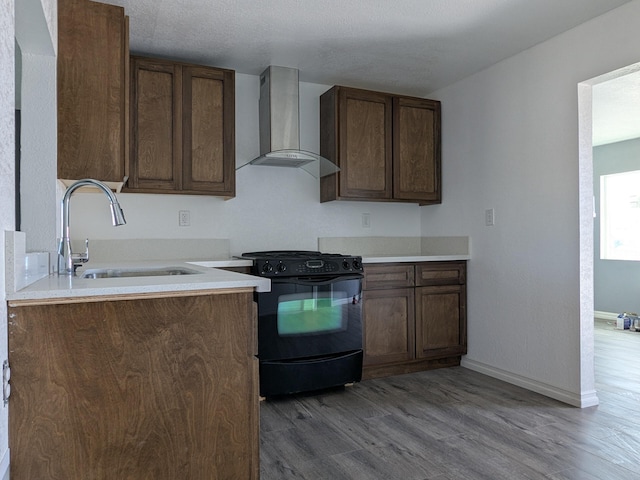 kitchen featuring black gas range oven, baseboards, wood finished floors, wall chimney exhaust hood, and a sink