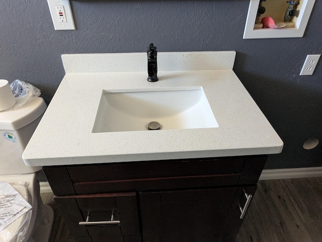 bathroom with a textured wall, baseboards, wood finished floors, and vanity