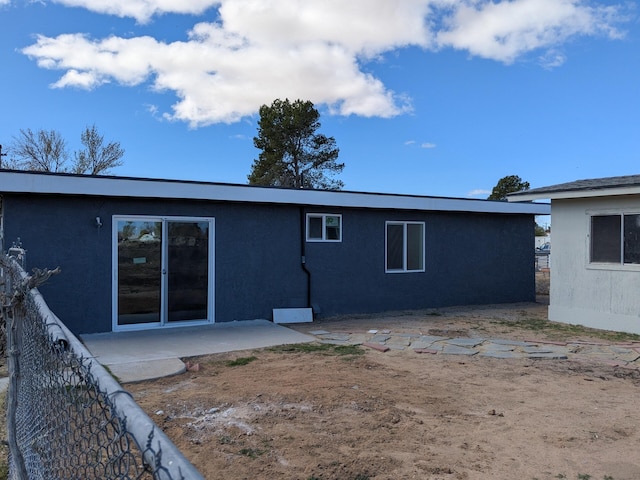 rear view of house with stucco siding, fence, and a patio area