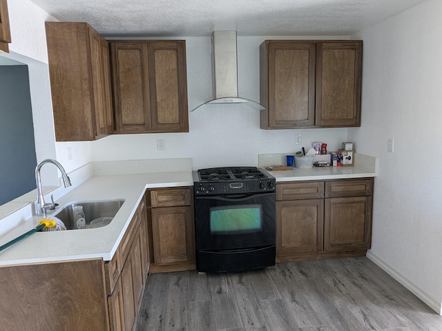 kitchen featuring light countertops, a sink, light wood-style flooring, gas stove, and wall chimney range hood