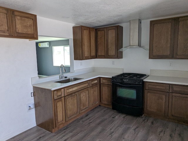 kitchen featuring light countertops, black range with gas stovetop, wall chimney exhaust hood, a sink, and dark wood-style floors