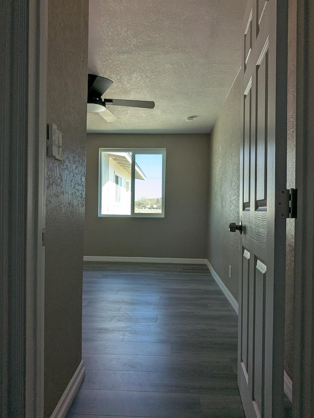 unfurnished room with a textured wall, baseboards, a textured ceiling, dark wood finished floors, and a ceiling fan