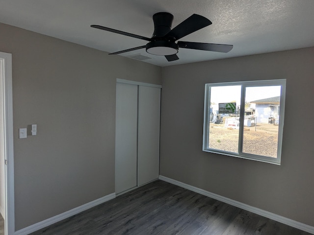 unfurnished bedroom with baseboards, a textured ceiling, dark wood-style floors, a ceiling fan, and a closet