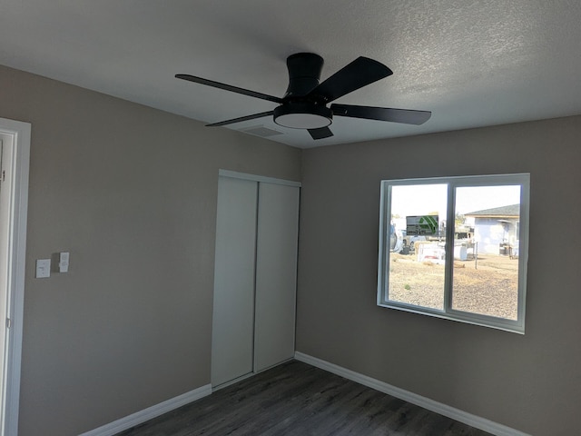 unfurnished bedroom with baseboards, a textured ceiling, dark wood-style floors, a ceiling fan, and a closet