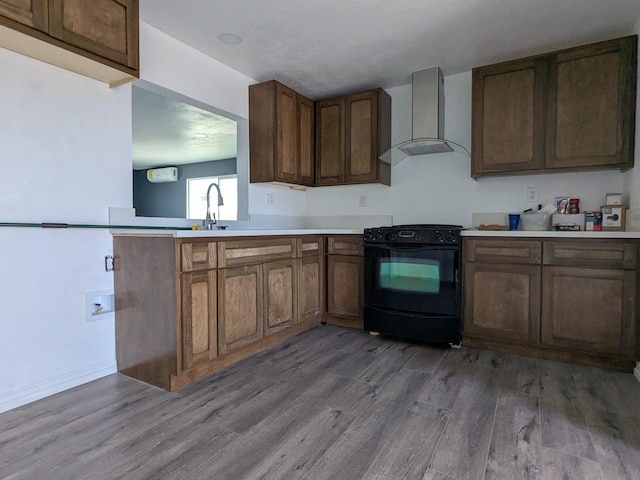 kitchen featuring black electric range oven, wall chimney range hood, light wood-style floors, and light countertops