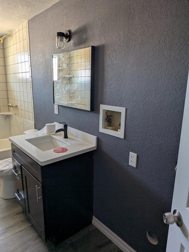 bathroom featuring baseboards, vanity, a textured wall, and a textured ceiling