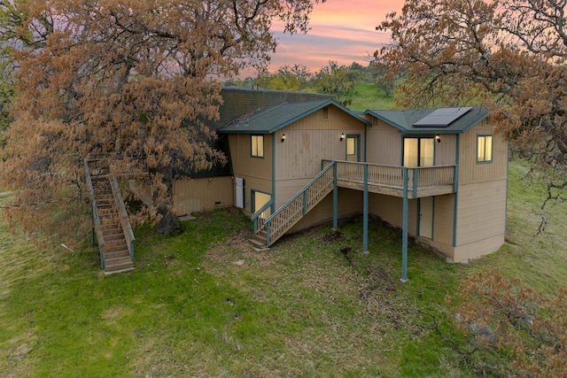 rear view of house with stairway, a lawn, solar panels, and a wooden deck