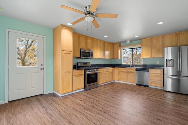 kitchen with dark countertops, appliances with stainless steel finishes, a sink, light wood-style floors, and recessed lighting