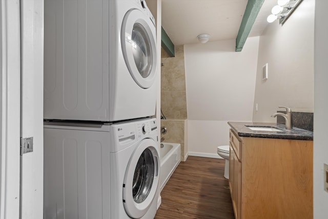 laundry area featuring a sink, dark wood finished floors, baseboards, visible vents, and stacked washer and clothes dryer