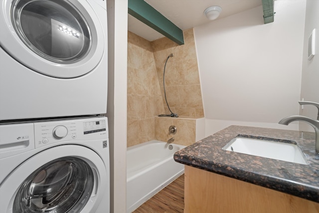 clothes washing area featuring a sink, stacked washing maching and dryer, and wood finished floors