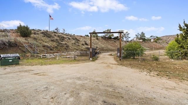 view of street with a gated entry, dirt driveway, and a rural view