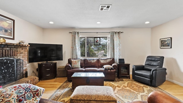 living room featuring visible vents, a brick fireplace, baseboards, recessed lighting, and light wood-style floors