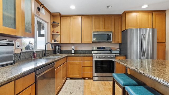 kitchen featuring open shelves, stainless steel appliances, dark stone counters, a sink, and light wood-style floors