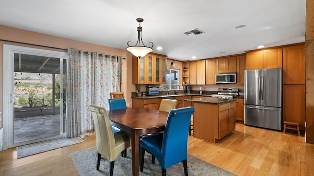 kitchen with visible vents, stainless steel appliances, a kitchen island, a sink, and brown cabinetry
