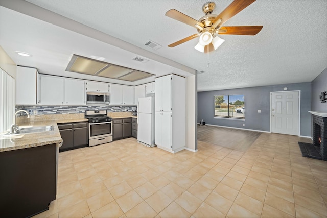 kitchen with white cabinetry, sink, a brick fireplace, light stone counters, and appliances with stainless steel finishes