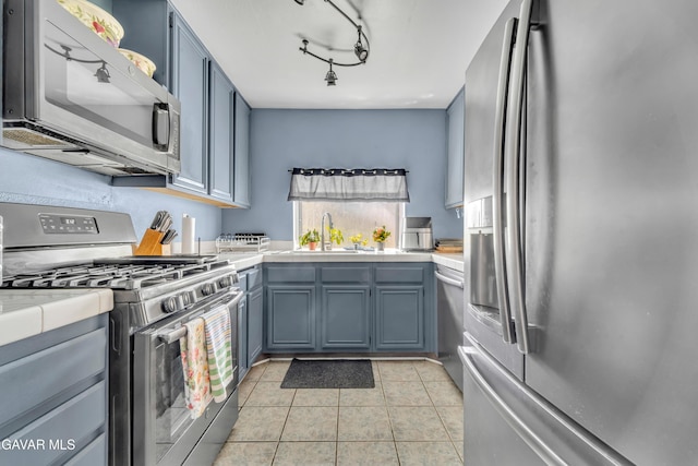 3628 Marilynn St, Lancaster, CA 93536 - kitchen with stainless steel appliances, tile countertops, light tile patterned floors, blue cabinetry, and rail lighting