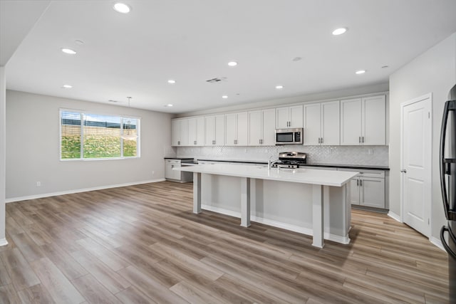 kitchen featuring light wood-type flooring, an island with sink, backsplash, recessed lighting, and stainless steel appliances