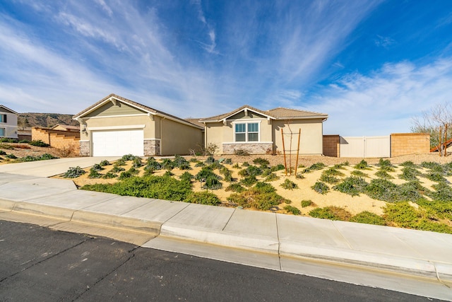 view of front of house featuring stucco siding, driveway, stone siding, fence, and a garage