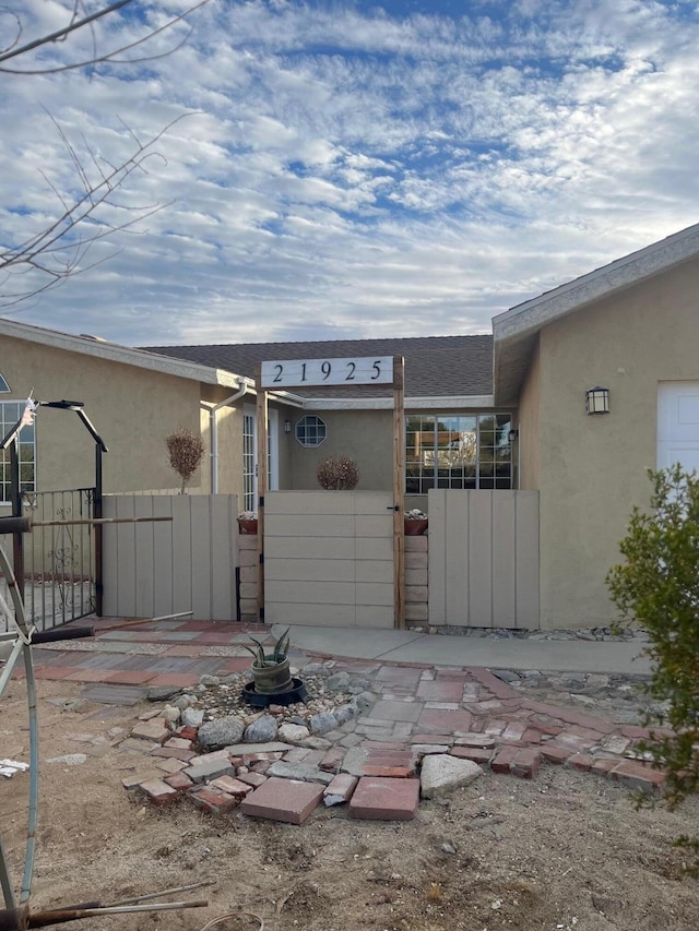 exterior space with stucco siding, fence, a shingled roof, and a gate