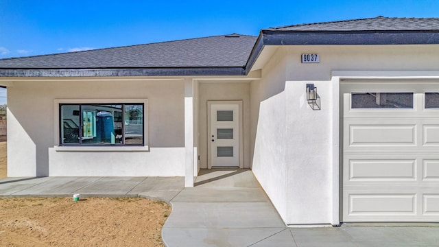 entrance to property featuring a garage, roof with shingles, and stucco siding