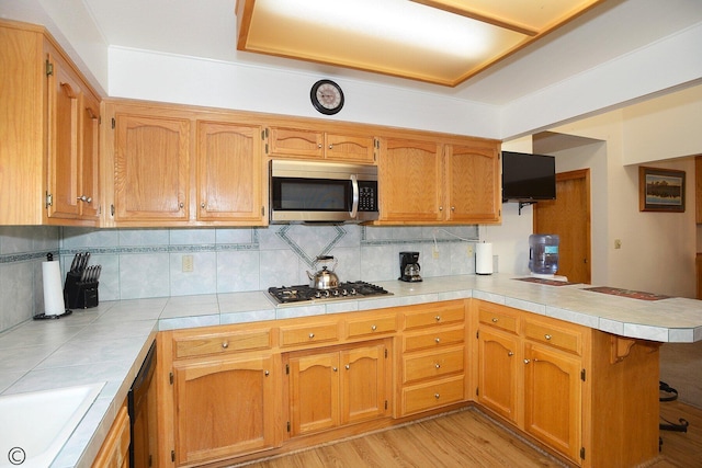 kitchen featuring backsplash, sink, light wood-type flooring, kitchen peninsula, and stainless steel appliances