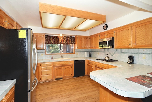 kitchen with sink, appliances with stainless steel finishes, tasteful backsplash, tile counters, and kitchen peninsula