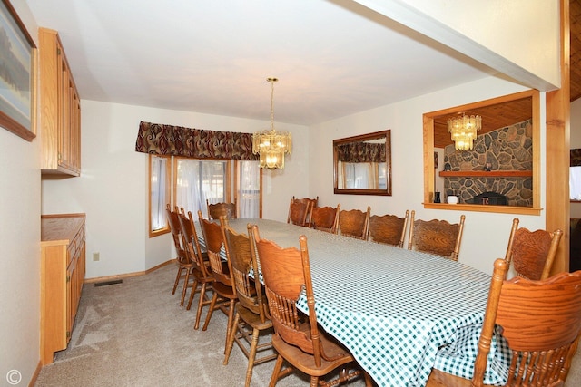 dining room with light colored carpet, a stone fireplace, and a notable chandelier