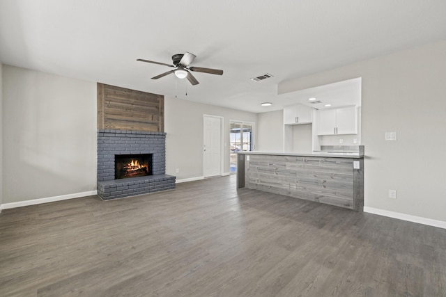 unfurnished living room with ceiling fan, a fireplace, and dark wood-type flooring