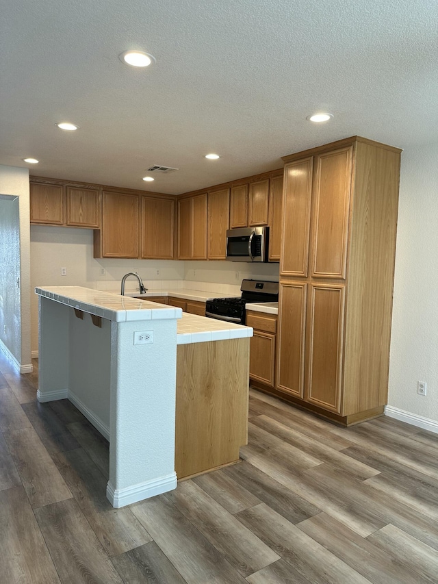 45559 Robinson Dr, Lancaster, CA 93535 - kitchen featuring stainless steel microwave, range with gas stovetop, tile counters, wood finished floors, and recessed lighting
